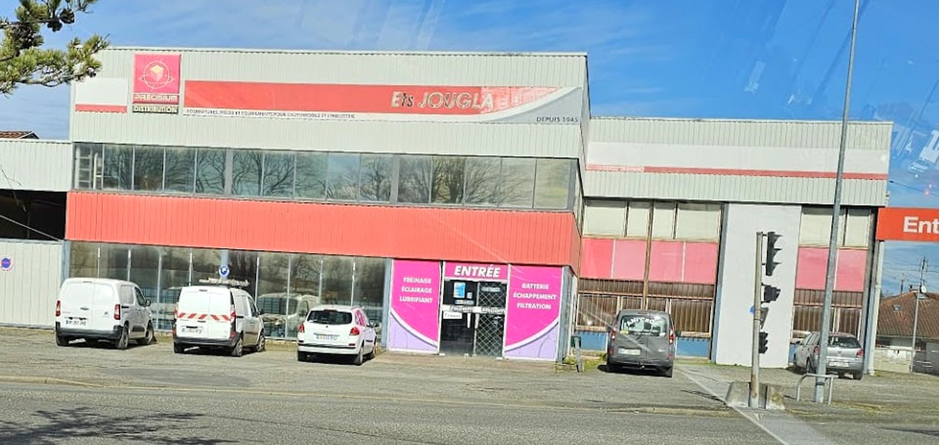 Le bâtiment des Etablissements Jougla vu depuis la route à Dax, avec l'enseigne rouge et l'entrée de l'atelier.